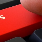 Success Red Button - Finger Pushing Button of Black Computer Keyboard. Blurred Background. Closeup View.